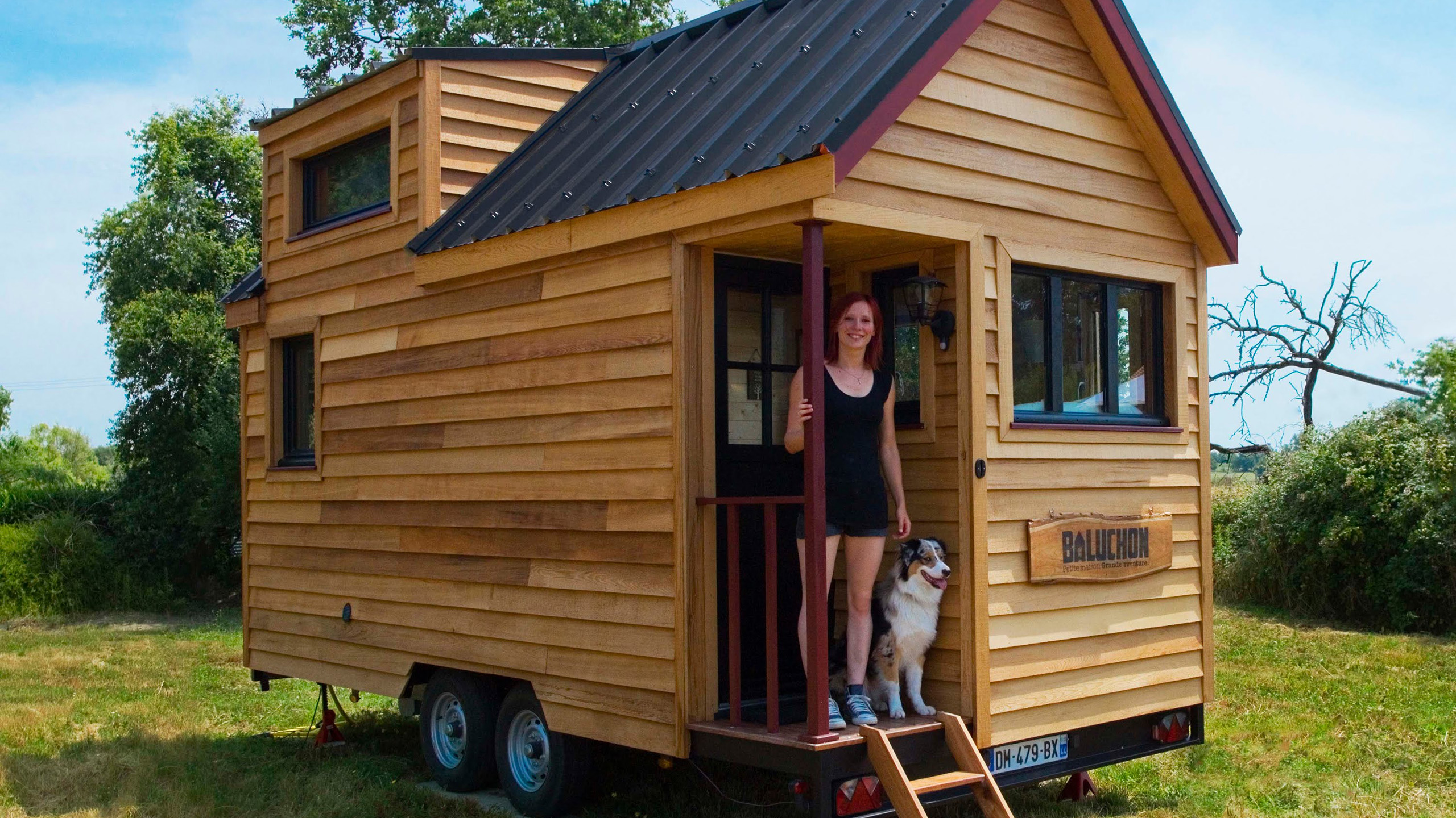 a very tiny house on wheels sitting in a green, grassy area